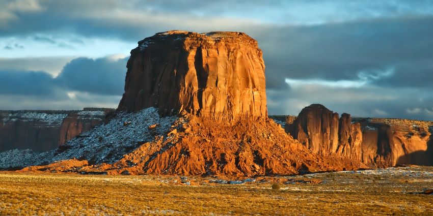 Snapshot strategies of a towering red rock formation rises majestically against a backdrop of blue skies and scattered clouds, showcasing a rugged landscape.