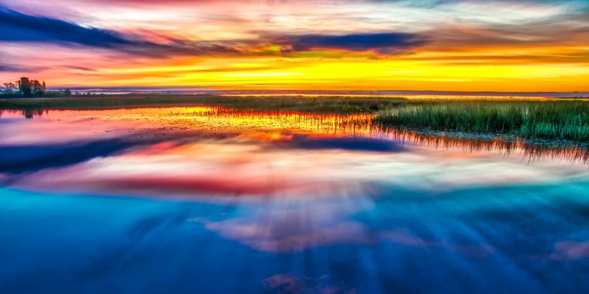 Shooting tips for a vibrant sunset casts brilliant colors across the water, reflecting shades of orange, pink, and blue in a serene landscape. Photography Tips From Industry Experts.