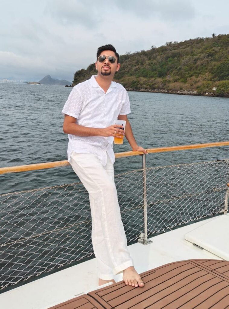 A man in a white outfit and sunglasses holding a drink, relaxing on a yacht.