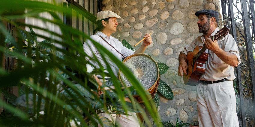 Two musicians playing folk music with a drum and guitar in a rustic setting.