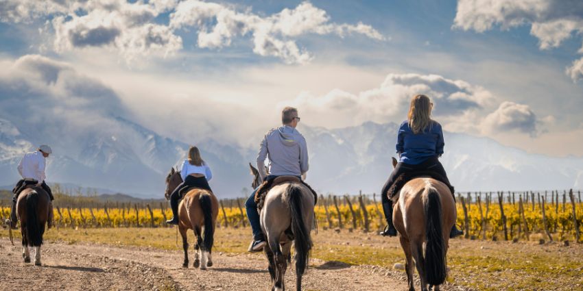 Travelers horseback riding through scenic vineyards in Argentina with mountains in the background.